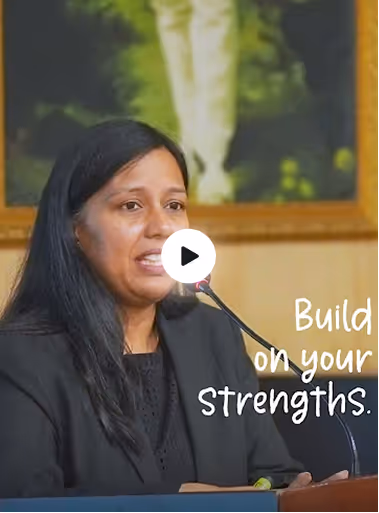 Woman speaking at a podium with a microphone, beside text saying 'Build on your strengths.'