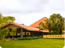 Building with a red tiled roof surrounded by green lawn and trees.