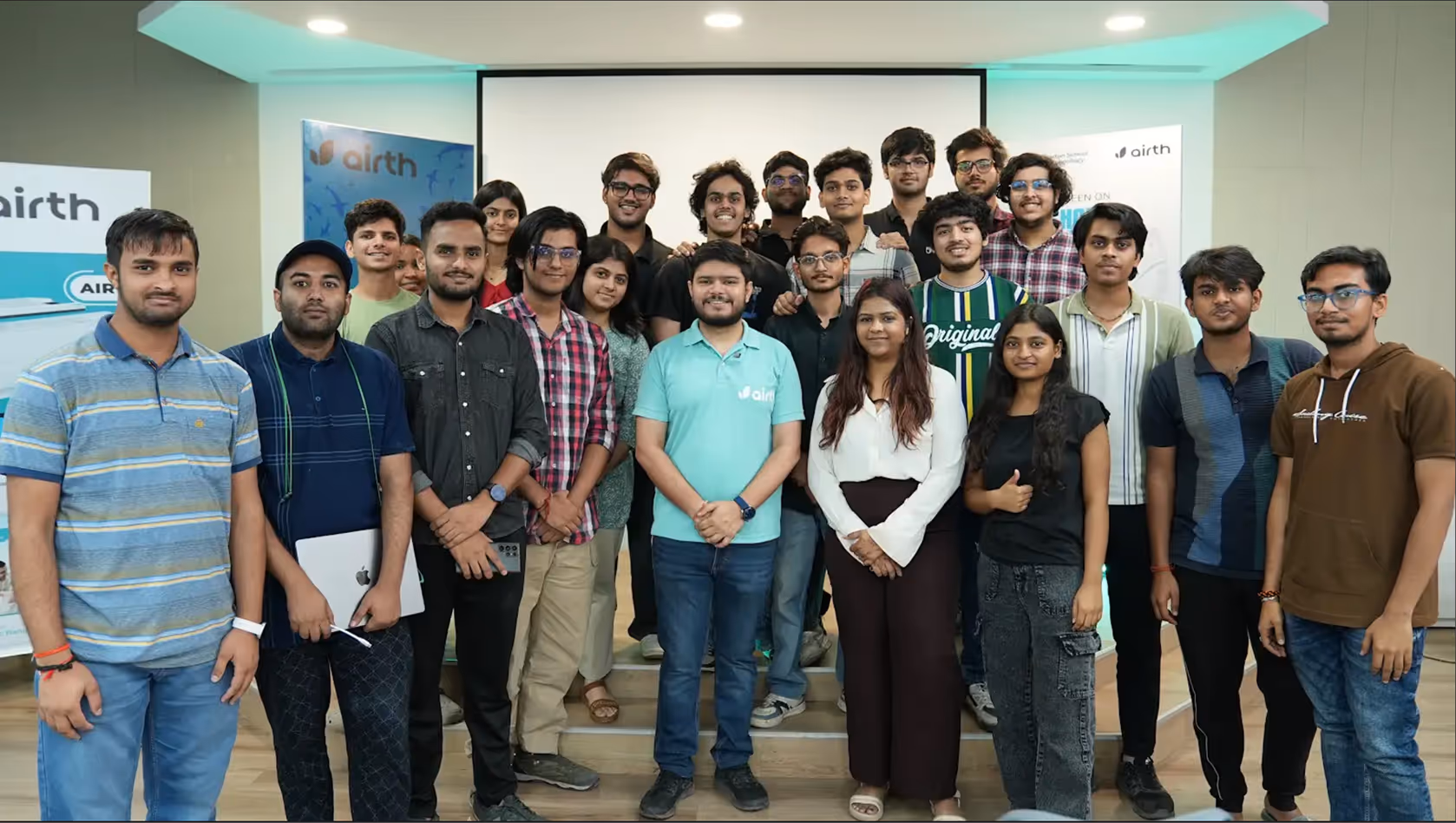 Group photo of a diverse team of young adults standing indoors in front of branded Airth banners.