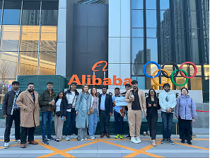 Group standing in front of the Alibaba sign with Olympic rings displayed
