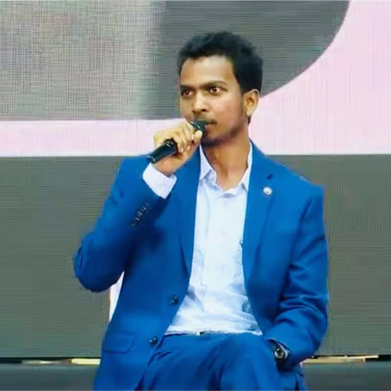 Man in a blue suit speaking into a microphone while seated.