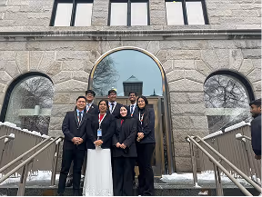 Five people in formal attire on the stone steps of a Harvard building