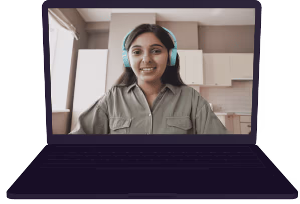 Smiling woman wearing teal headphones looking at the camera on a laptop screen in a kitchen setting.