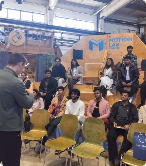 Group seated on tiered benches listening to a speaker indoors