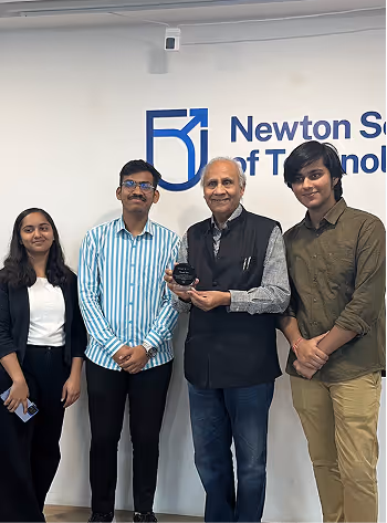 Four people standing indoors in front of a Newton School of Technology sign.