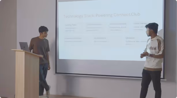 Two students presenting a venture pitch in front of a large projection screen.
